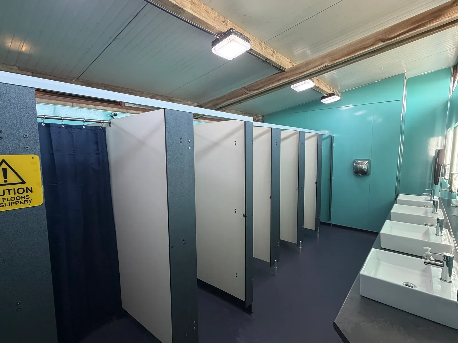 Inside the block: a row of shower and toilet cubicles, one with a shower curtain, and basins along the wall on the right.